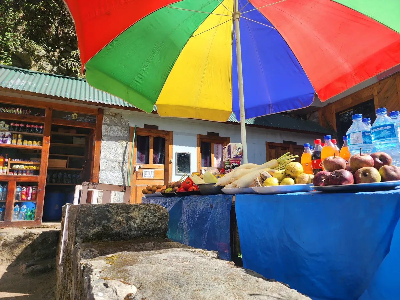 A trailside stall selling fruit and drinks under a bright umbrella.