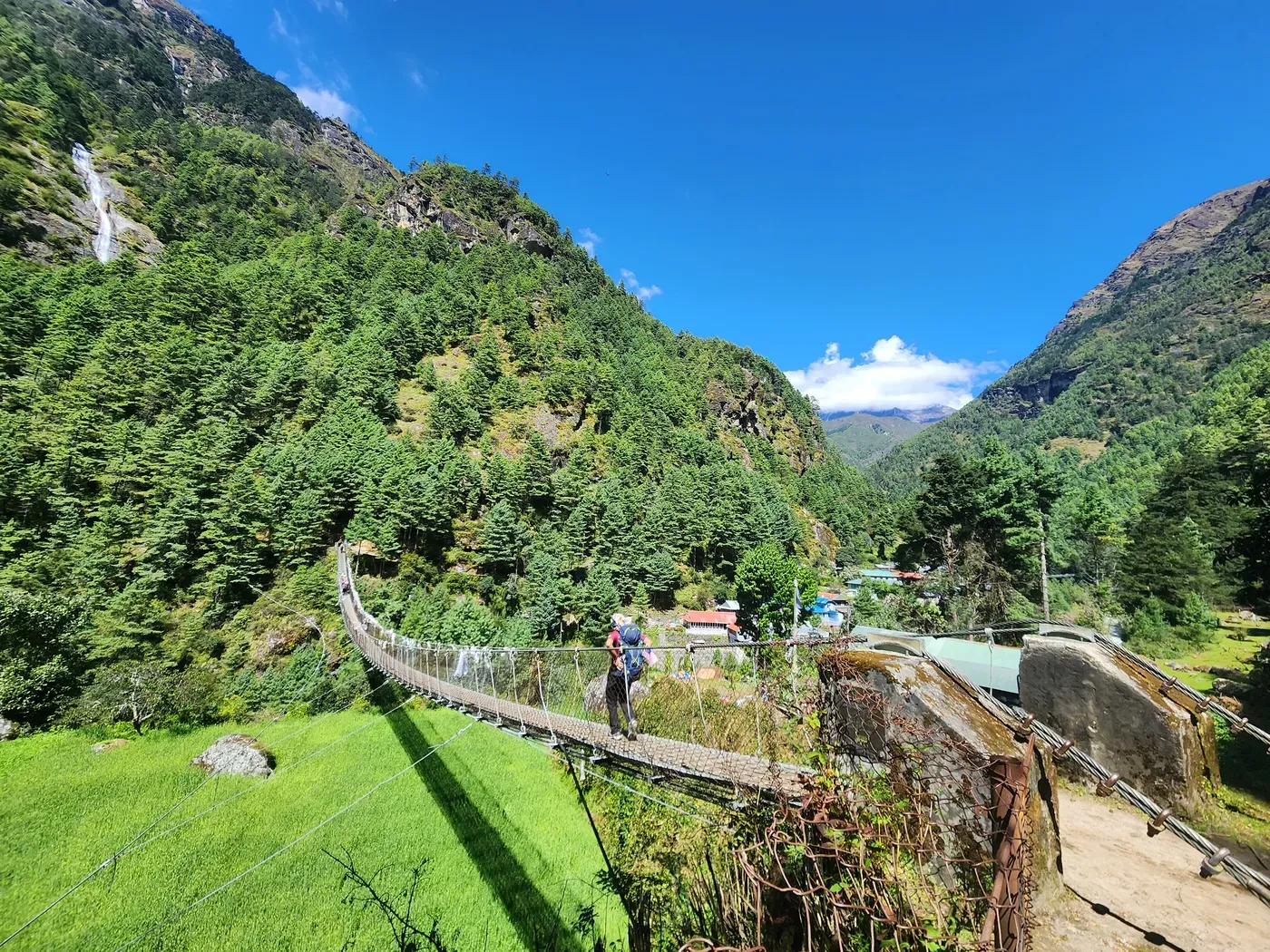 A suspension bridge strung with prayer flags on the lower Everest trail, green terraces and forested valley beyond.
