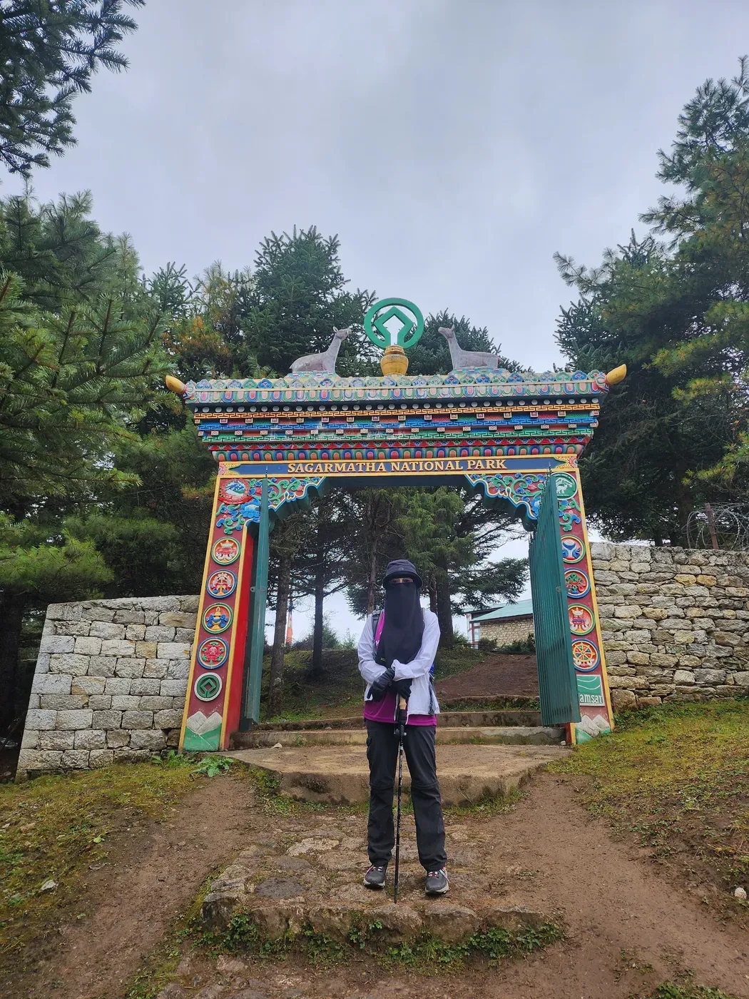 A trekker standing under an ornately painted Buddhist kani gateway arch on the trail.