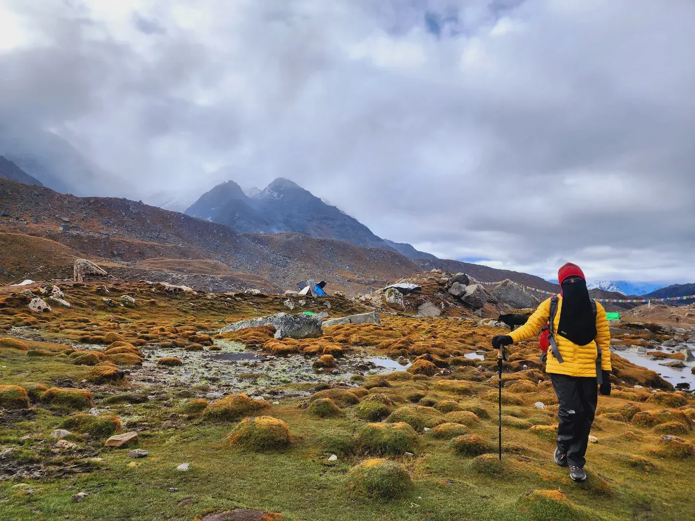 A trekker on a long alpine stretch of trail, snow peaks ahead.