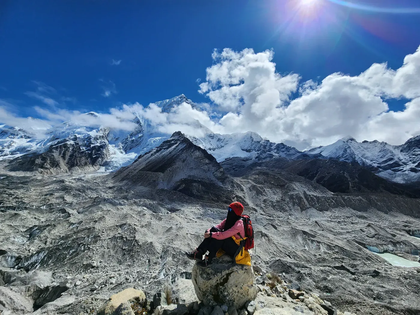 A trekker resting on a boulder high on the Everest Base Camp trail, a wall of Himalayan peaks behind.