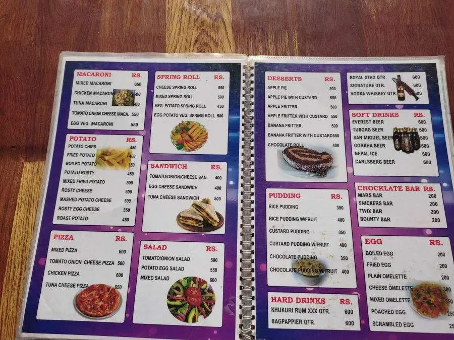 A laminated teahouse menu on the Annapurna Base Camp trail, prices in Nepali rupees — sections for macaroni, potato, pizza, spring rolls, sandwiches, salad, desserts, puddings, drinks and eggs.