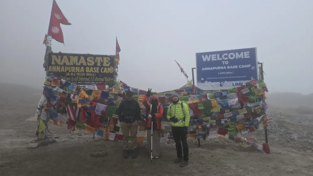 Trekkers at the Annapurna Base Camp sign (4,130 m), prayer flags and the Nepal flag in the mist